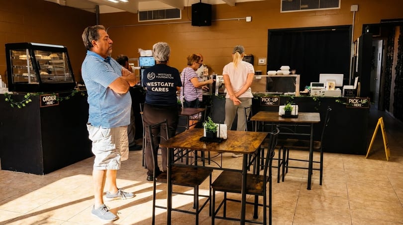 Customers wait in line at a restaurant counter with "Order Here" and "Pick-Up Here" signs.