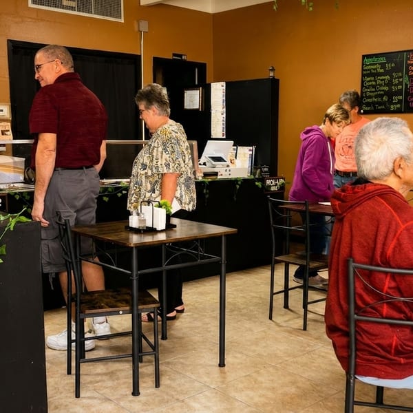 Customers ordering and dining in a casual restaurant with a menu board on the wall.