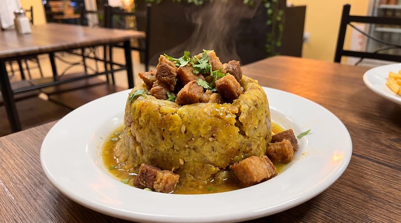 Steaming mofongo with chunks of pork and cilantro on a white plate at a restaurant.